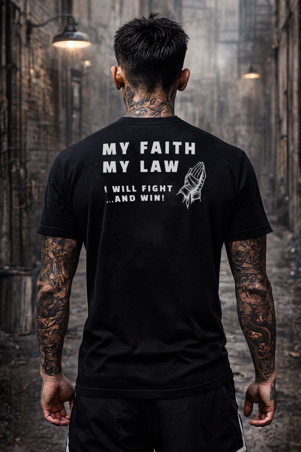 Person wearing a black t-shirt with text and a design on the back, standing in an industrial setting.