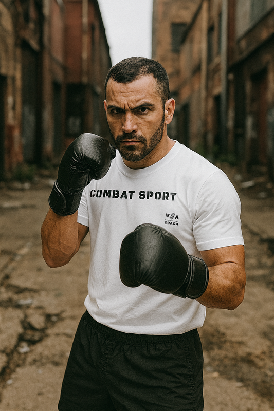 Man in a white 'Combat Sport' t-shirt with black boxing gloves in an alleyway.