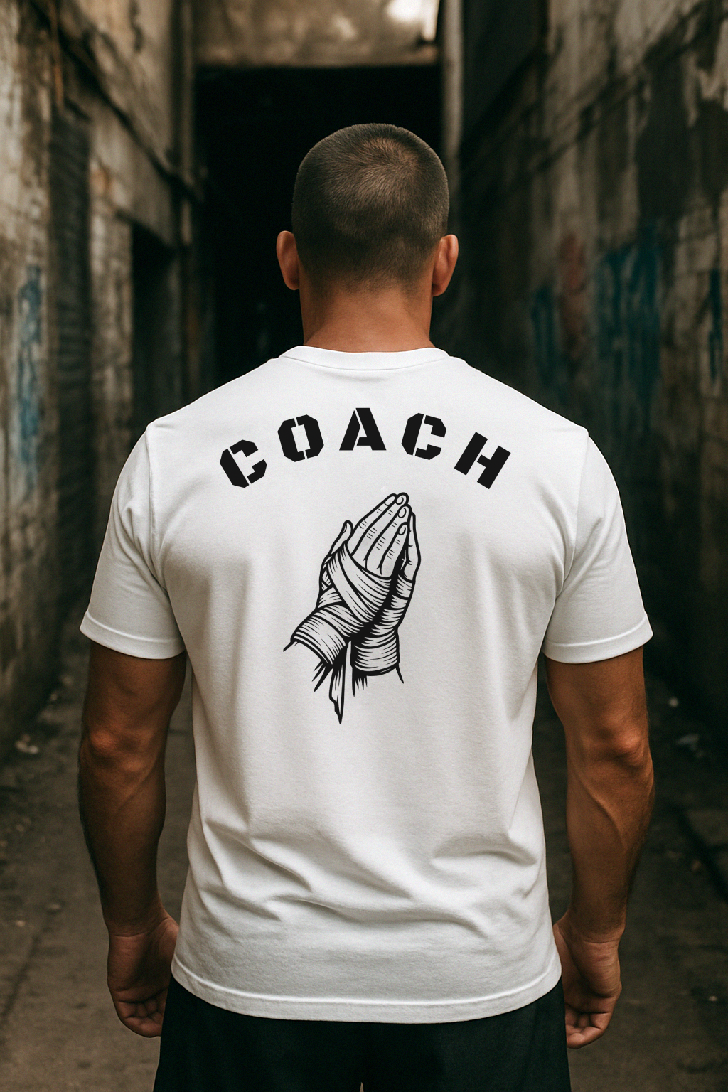 Man wearing a white t-shirt with 'COACH' and a graphic design in an alleyway.