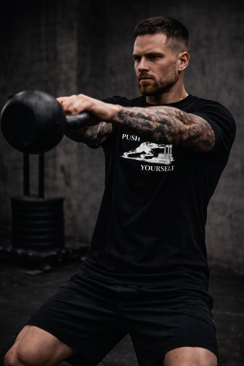 Man lifting a kettlebell wearing a black t-shirt with 'Push Yourself' graphic.