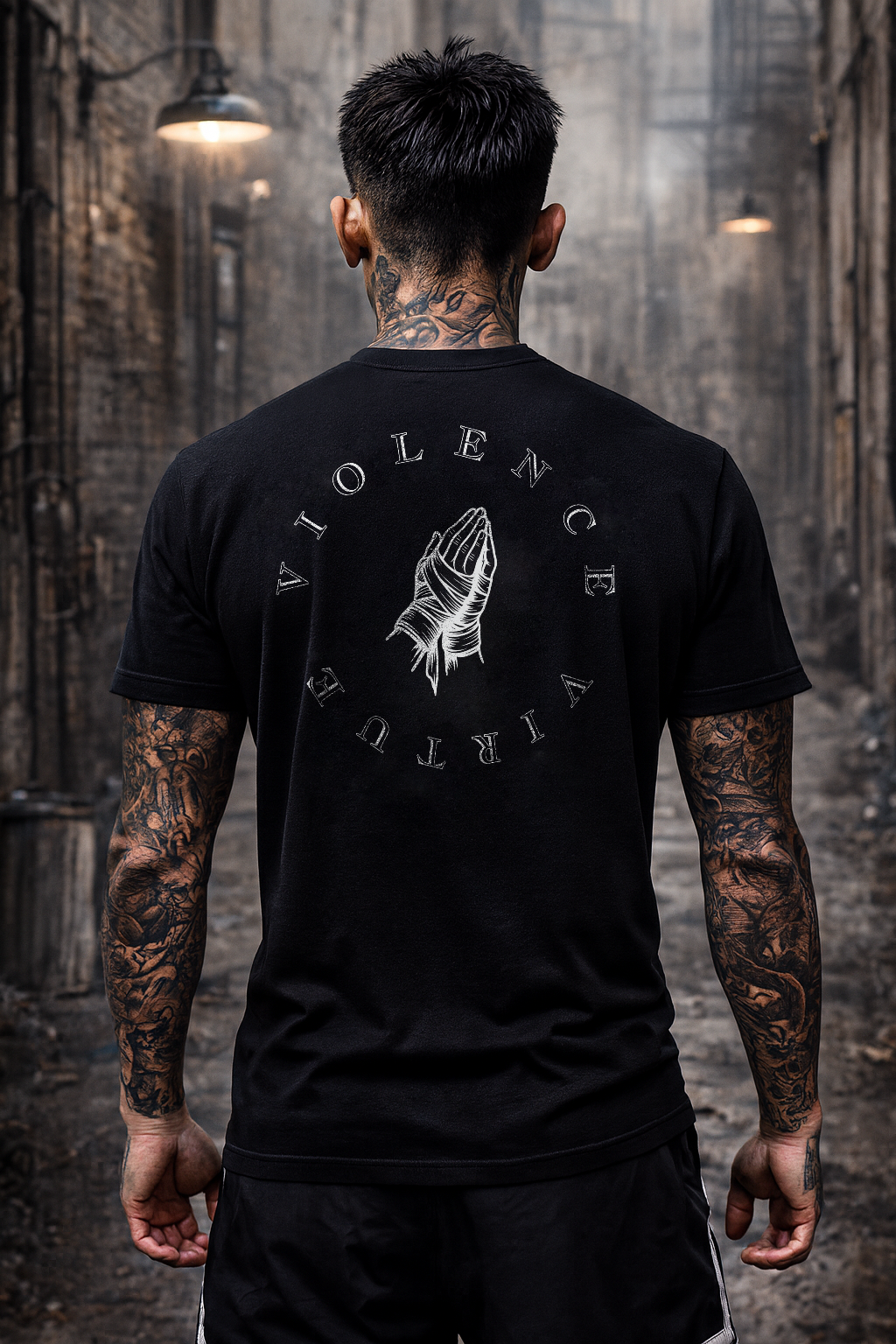 Person wearing a black t-shirt with a graphic design and text, standing in an industrial setting.